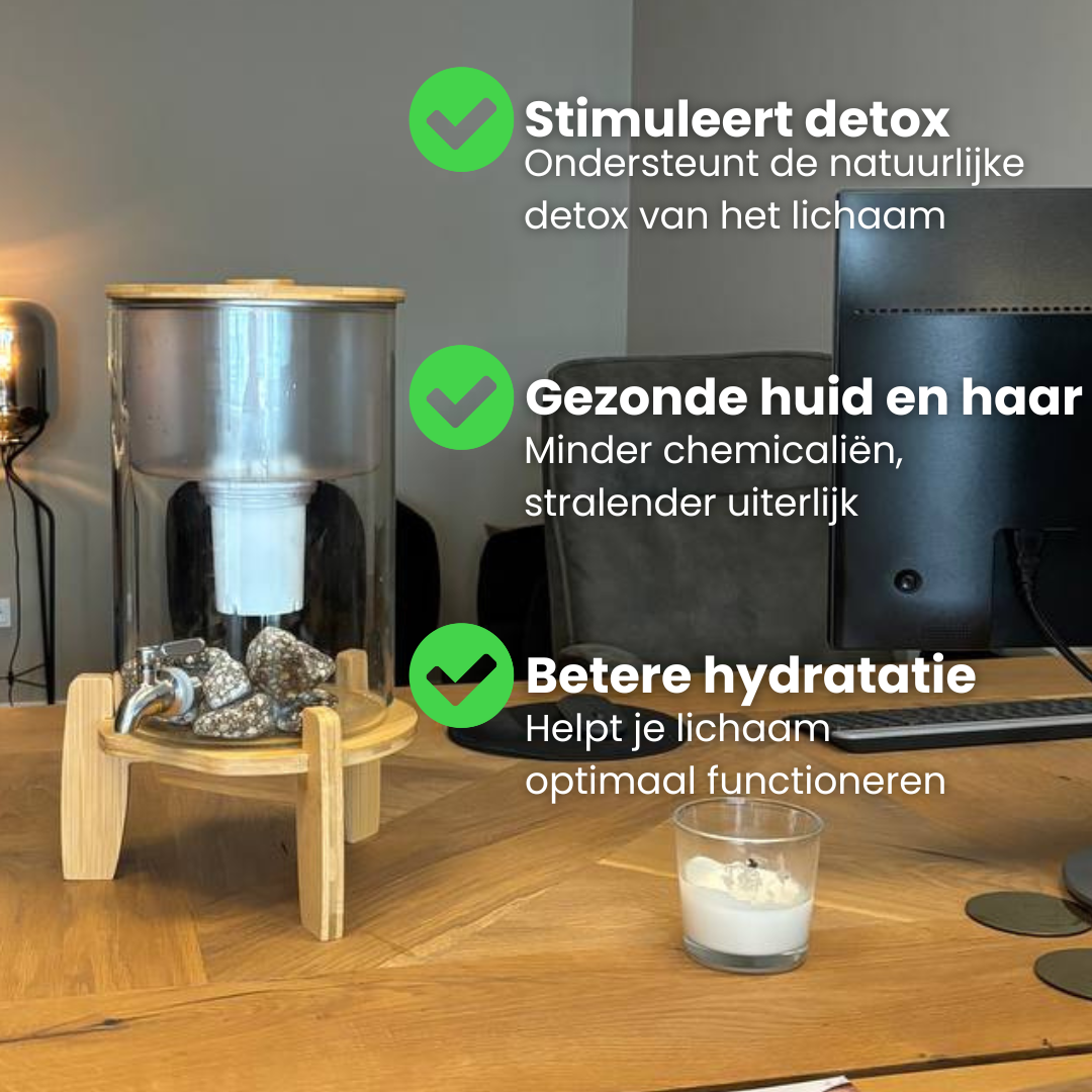 Glazen waterfilter op houten standaard op een bureau, naast een computer en een glas water. In beeld staan teksten met vinkjes. Stimuleert detox en ondersteunt de natuurlijke detox van het lichaam. Gezonde huid en haar door minder chemicaliën. Betere hydratatie voor optimaal functioneren van het lichaam.